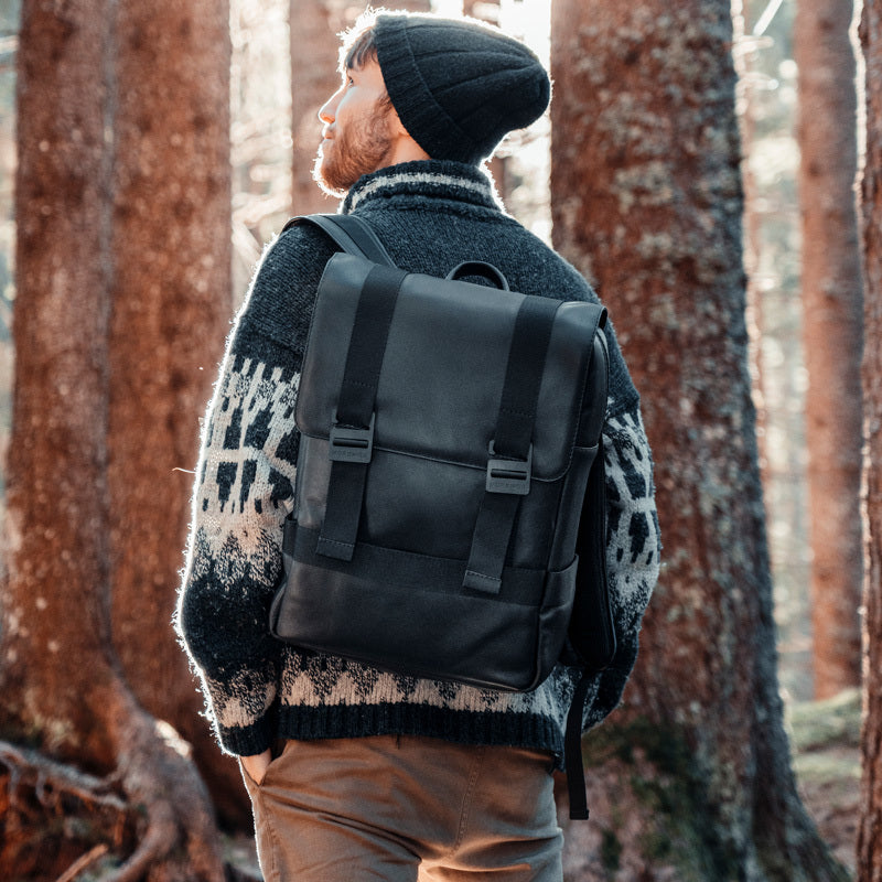 Nordweg black leather backpack worn near a brick wall in a rear carry lifestyle photo