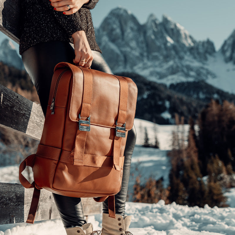 Nordweg caramel brown leather backpack held at a mountain lake overlook in a travel lifestyle photo