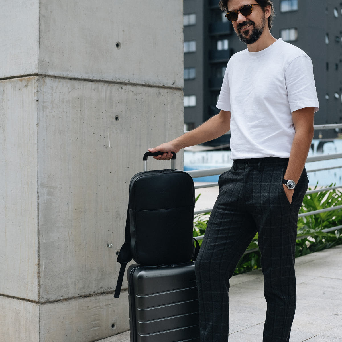 Man standing with the Black Slim Workplace backpack secured on a rolling suitcase