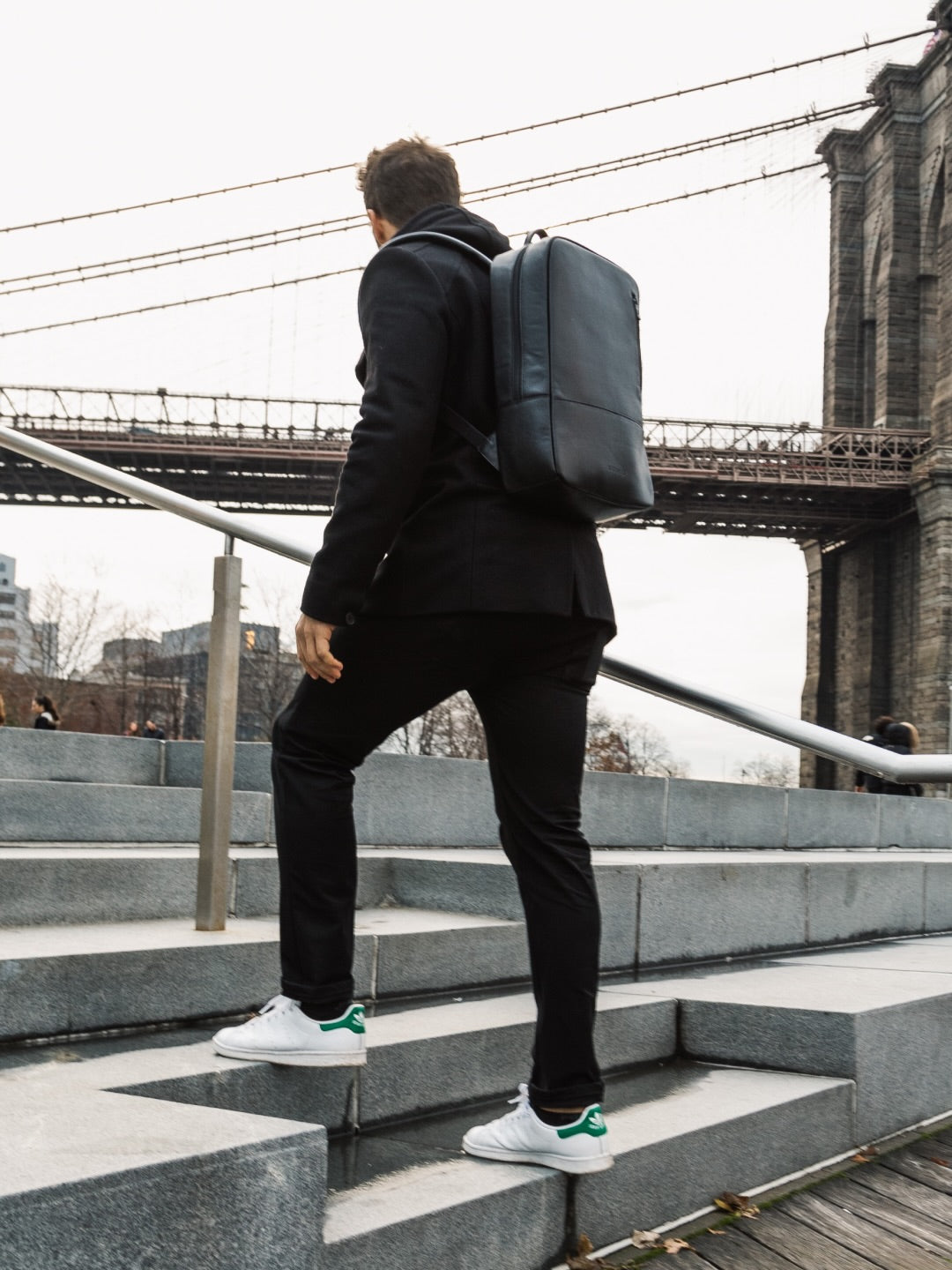 Black Nordweg Nomad Laptop Backpack worn on steps beside a city bridge.