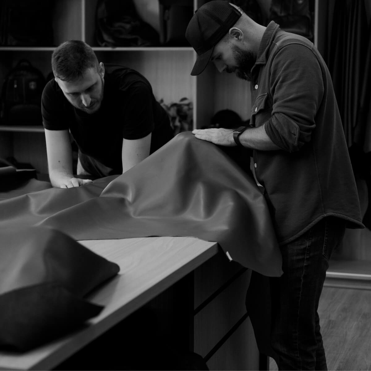 Two Nordweg artisans inspecting a large leather hide on a workshop table, homepage craft story image