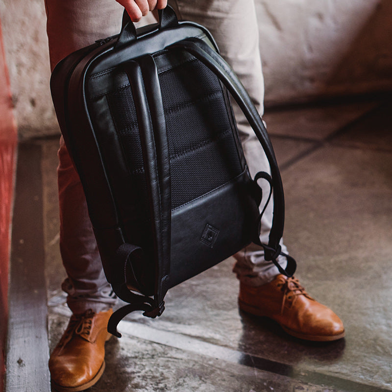 Nordweg black leather backpack beside boots on the floor in a close lifestyle photo