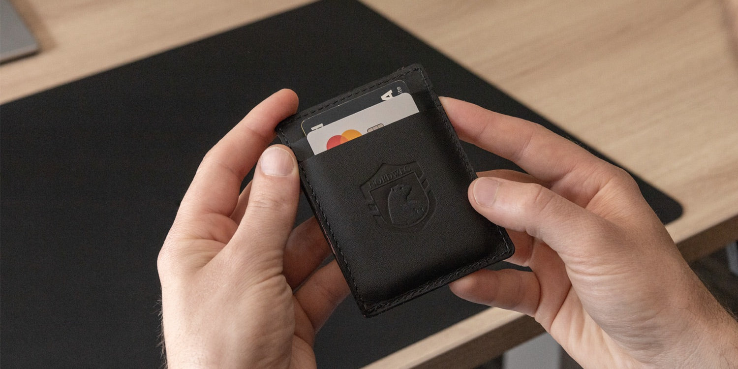 Black Nordweg leather cardholder wallet with cards, held above a black desk pad for the personal style collection