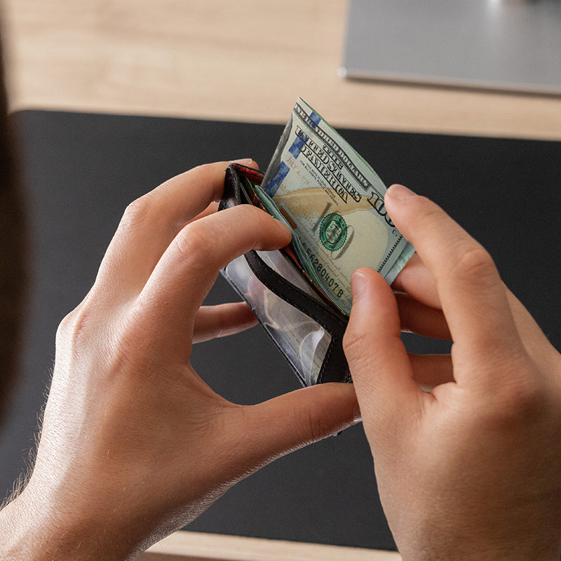 Nordweg black leather wallet open in hand with cash and cards at a desk