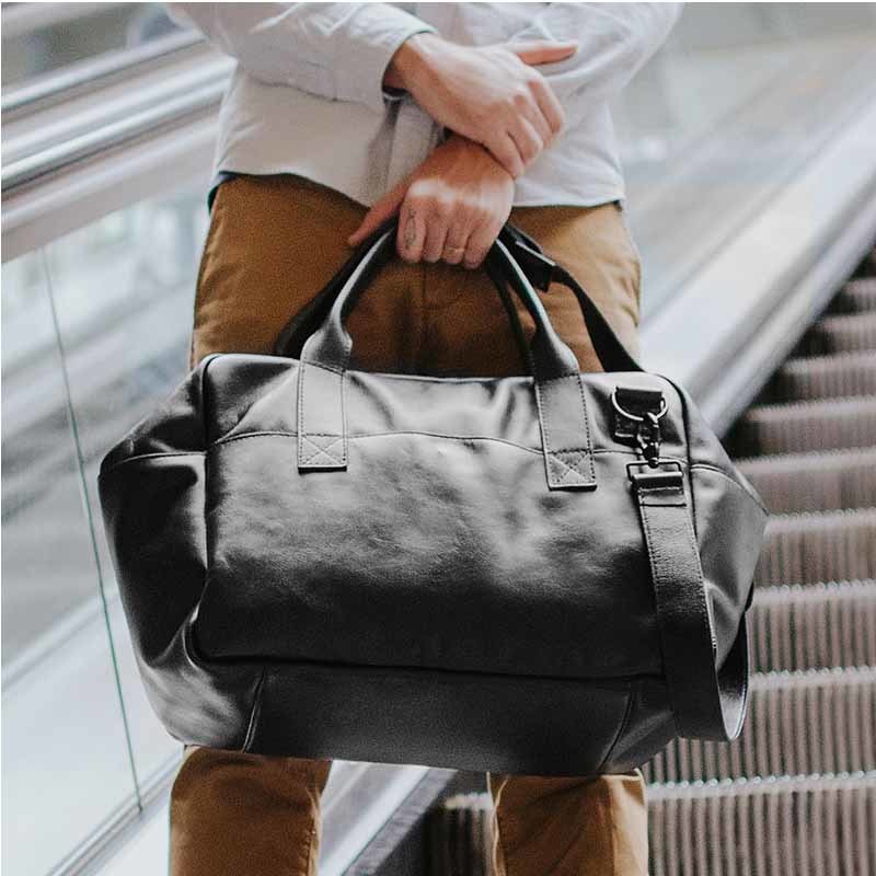 Nordweg black leather weekender duffel carried in front of an escalator