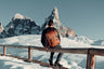 Nordweg Dolomites leather travel backpack in Caramel beside a snowy mountain railing, SKU NW101.CA, GTIN 7898571001044