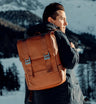 Nordweg Dolomites leather travel backpack in Caramel worn near a snowy mountain lake, mobile crop