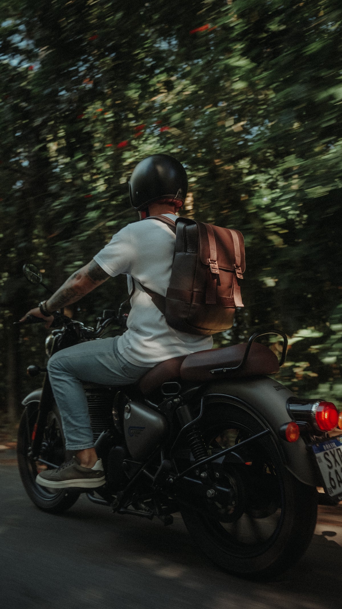Brown Nordweg Dolomites backpack worn on a motorcycle ride along a tree-lined road