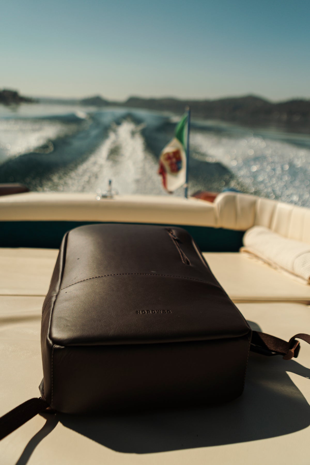 Coffee Nordweg Nomad backpack on a sunlit boat seat, with open water in the distance