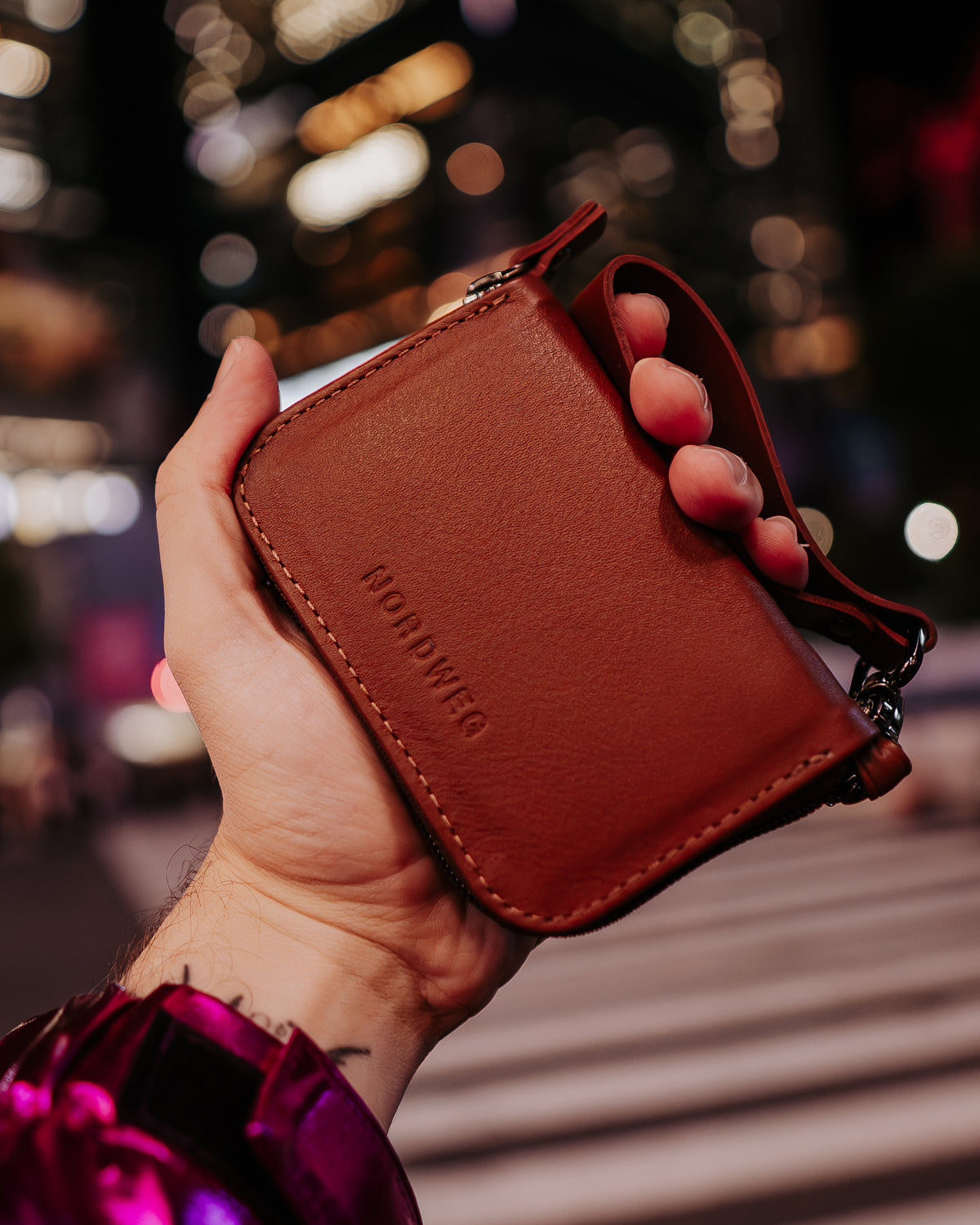 Brown Nordweg leather wallet held in a hand against softly lit city streets