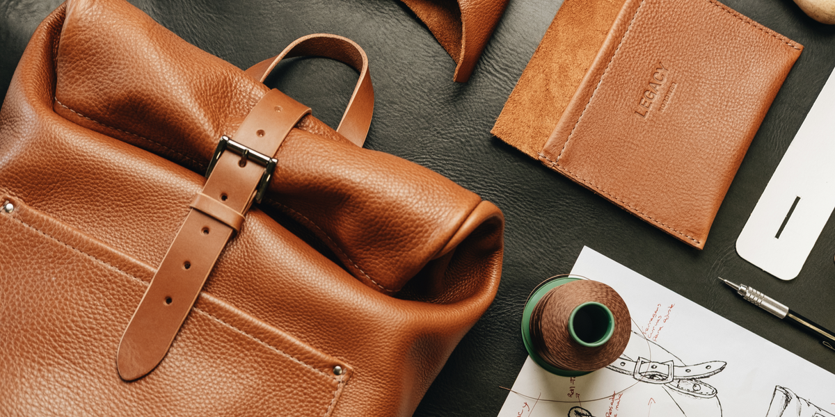 Caramel leather bag and wallet with thread and design sketches on a black workshop table