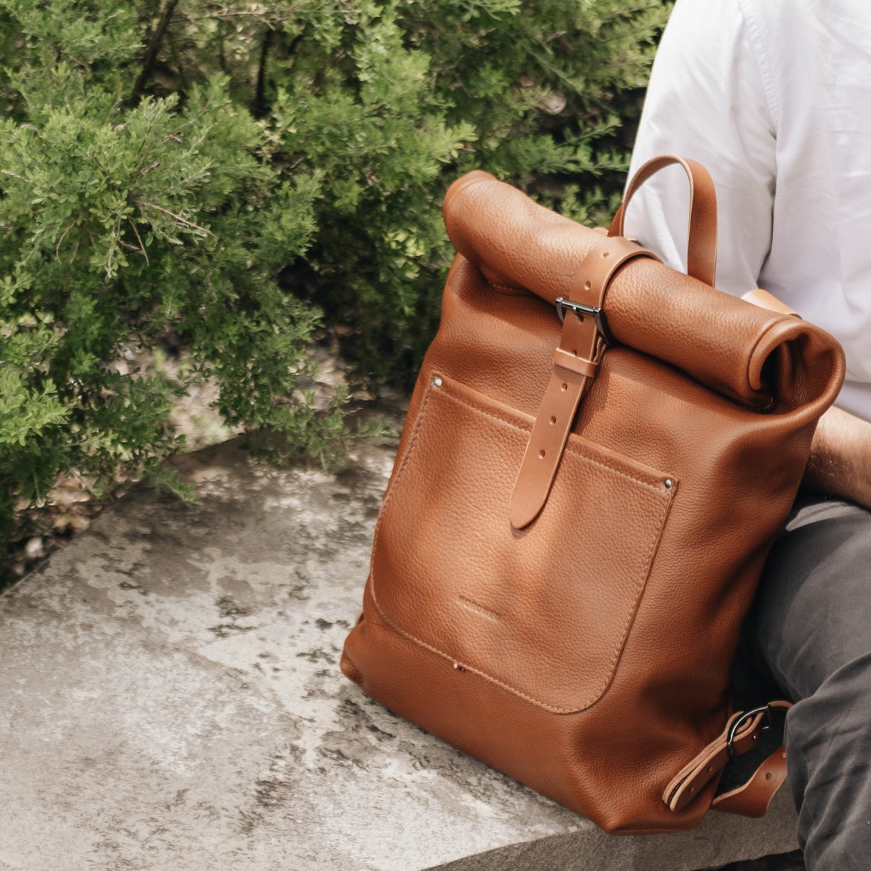 Legacy leather backpack in cognac beside a seated traveler