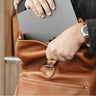 Hand inserting laptop into the main compartment of the Nordweg Legacy Leather Backpack in cognac