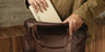 Hand placing a weekly planner into the top opening of the Nordweg Legacy Leather Briefcase in espresso