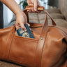 Hand placing a passport into the front pocket of the Nordweg Legacy Leather Duffel Bag in cognac