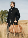 Cognac Nordweg Legacy leather duffel carried by hand in a grass field, SKU NWL002.CG, GTIN 7898571002300