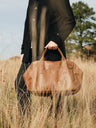 Cognac Nordweg Legacy leather duffel carried by hand through a grass field, SKU NWL002.CG, GTIN 7898571002300