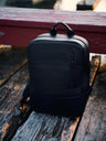 Black Nordweg Nomad leather laptop backpack displayed on a weathered waterfront dock in Canada