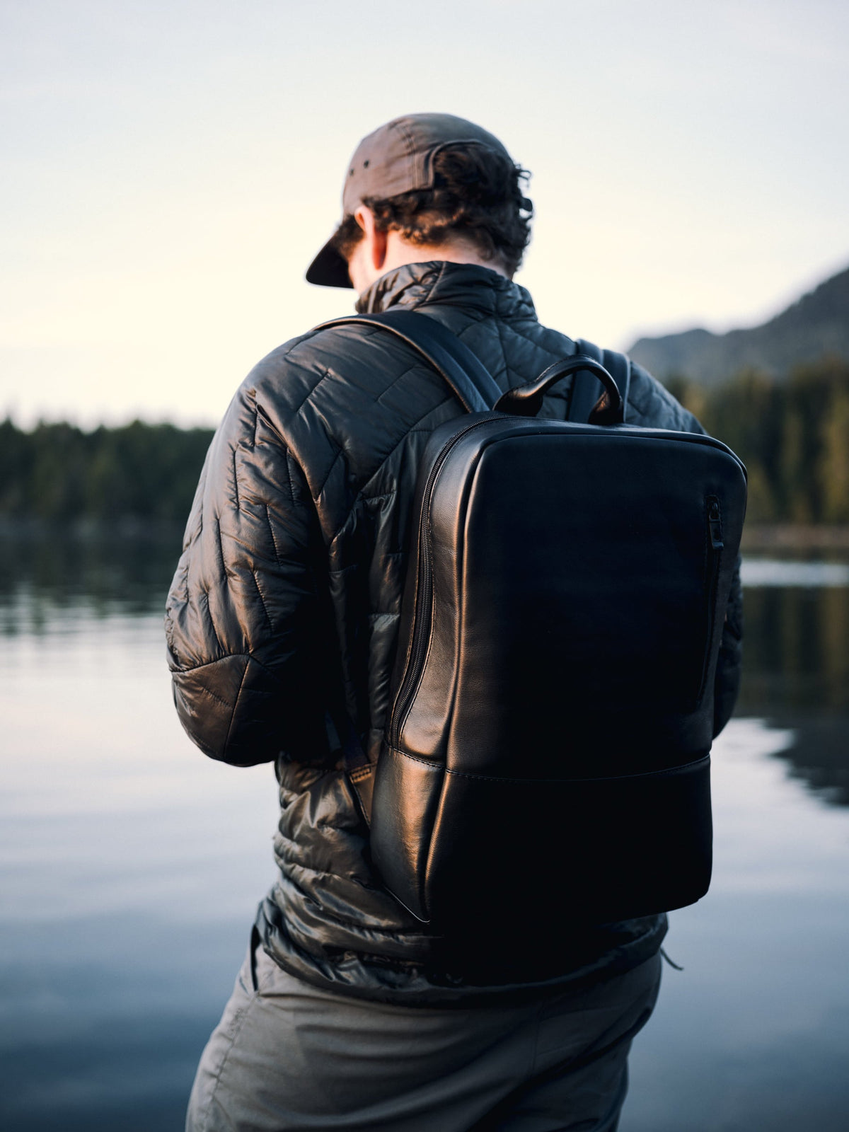 Man wearing a black Nordweg Nomad leather laptop backpack, standing beside calm water at a Canadian marina