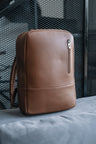 Caramel Nordweg Nomad leather laptop backpack displayed on a gray sofa
