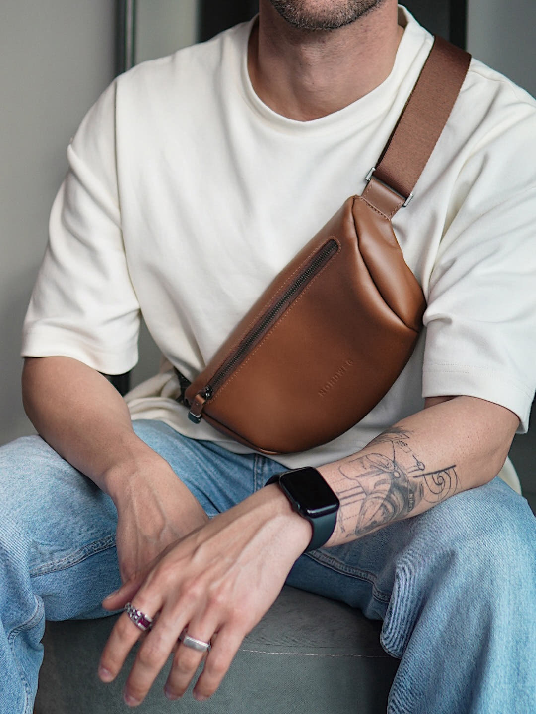 Caramel Nordweg Pulse leather sling bag worn across the chest while seated indoors, SKU NW112.CA, GTIN 7898571002232