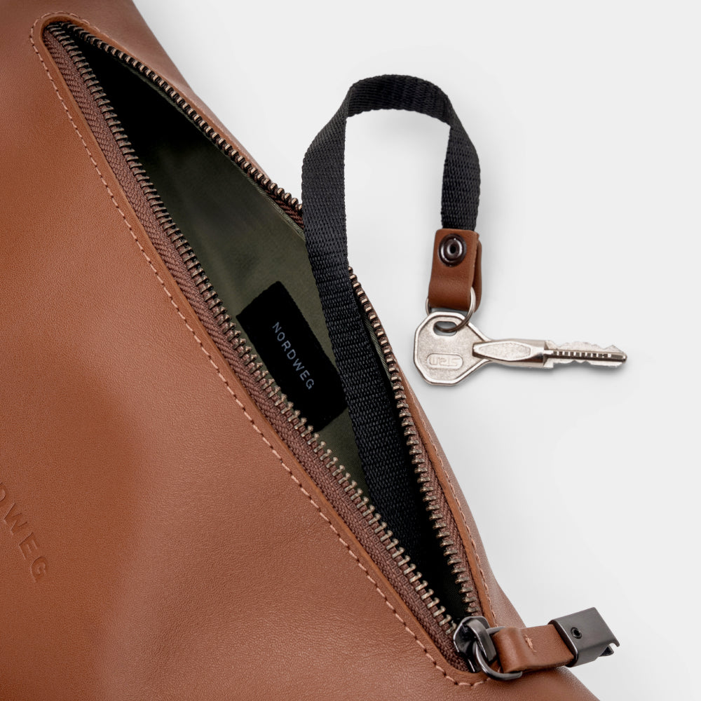 Open caramel Pulse leather sling bag showing top zipper and key leash detail