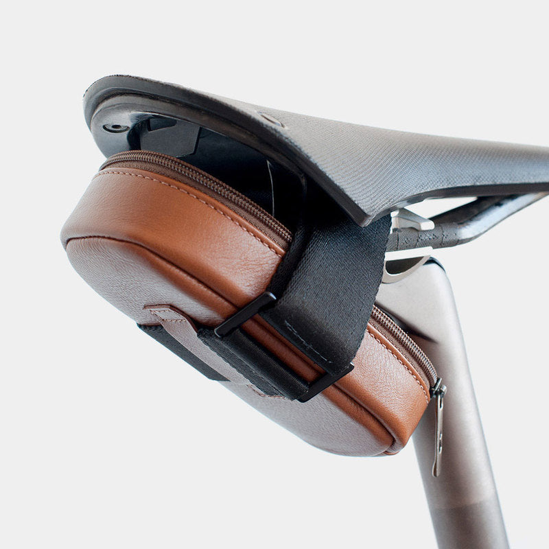 Caramel Nordweg Serra leather bicycle saddle bag installed under a bike seat with black attachment strap, SKU NW090.CA, GTIN 7898571000955