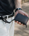 Black Nordweg Traveler Pro leather zip wallet held with its wrist strap clipped at the waist