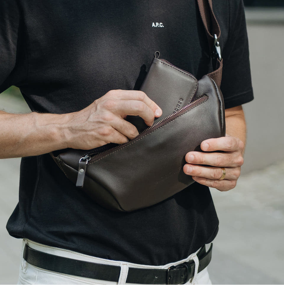 Coffee Nordweg Traveler Pro leather zip wallet shown beside a larger sling bag for size, SKU NW110.IC