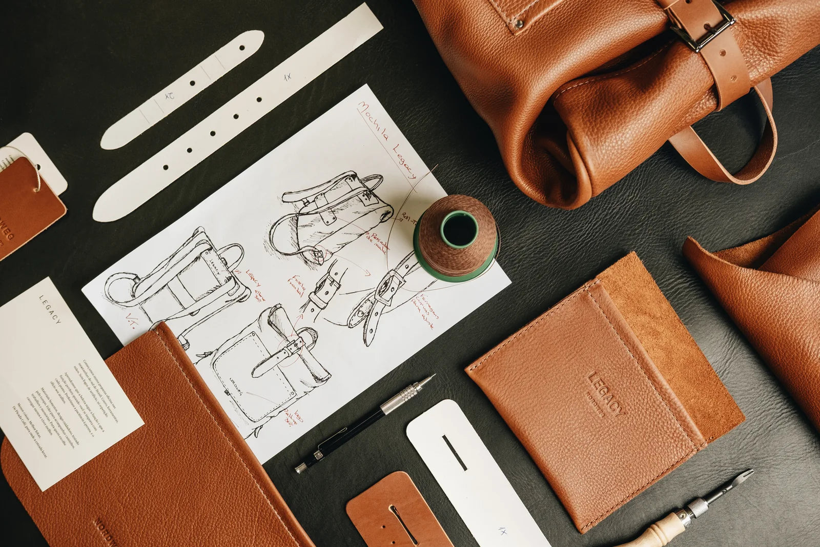 A caramel leather bag beside drawings, pattern pieces and workshop tools