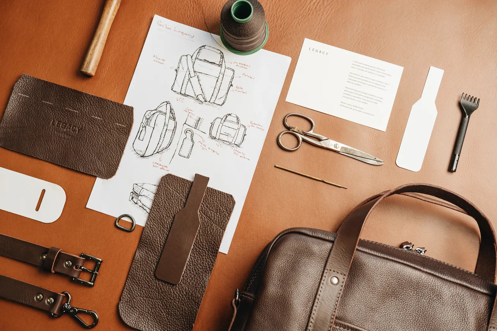 Brown leather components, scissors, thread and a bag drawing on the workbench