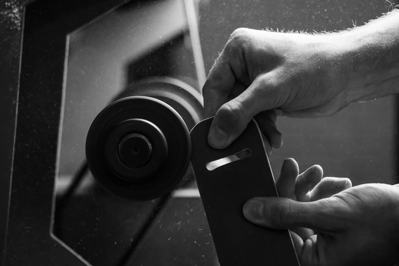 Hands guiding the edge of a leather component against a finishing wheel