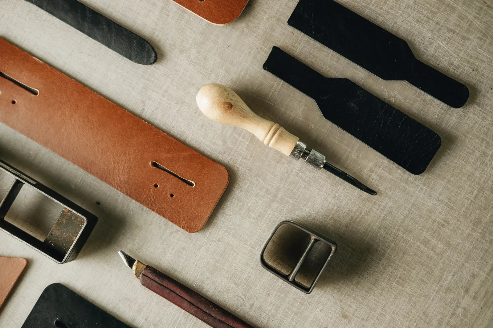 Leather components, hand tools and metal hardware laid out on the workshop table