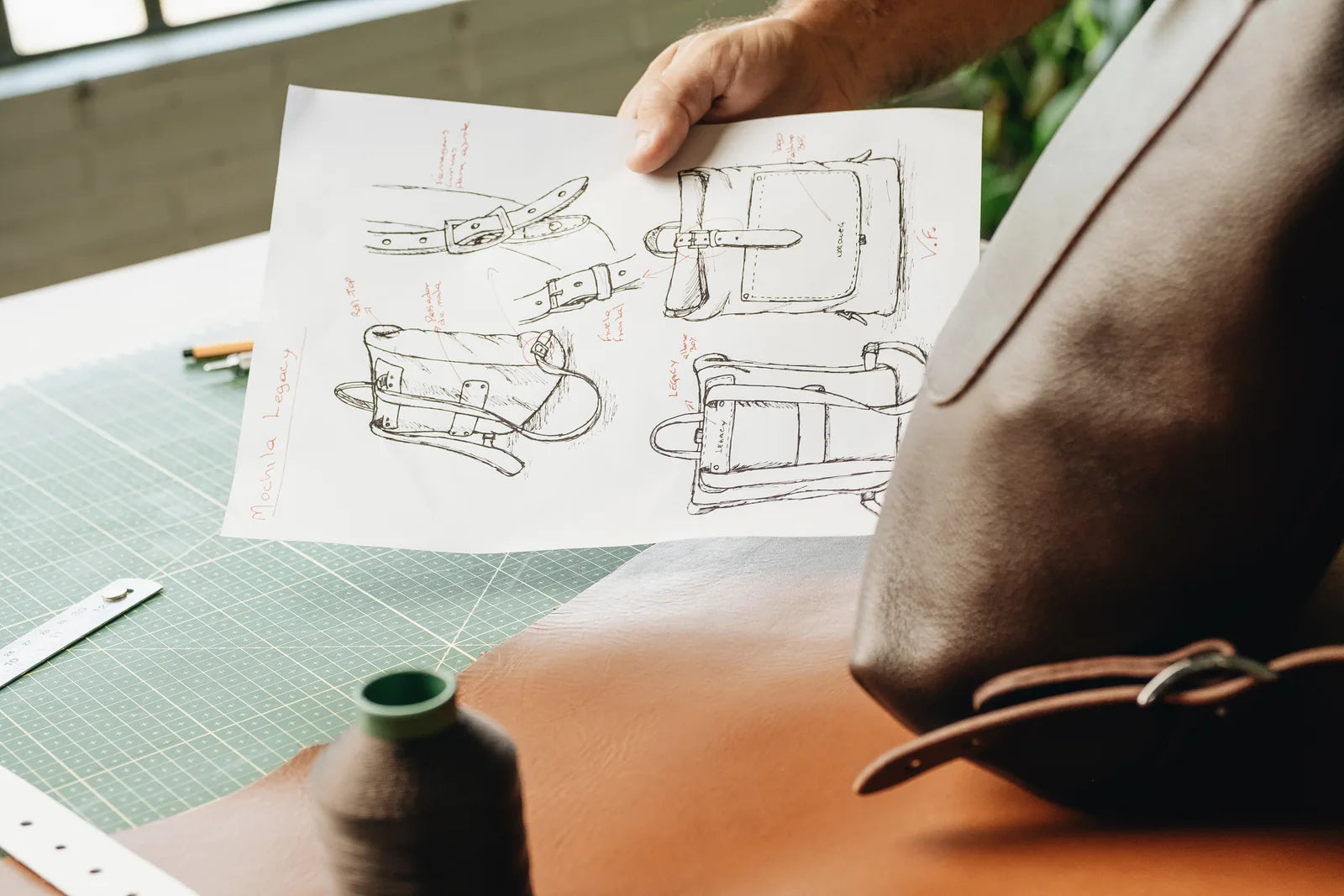 A maker holding a technical bag drawing beside the leather pieces