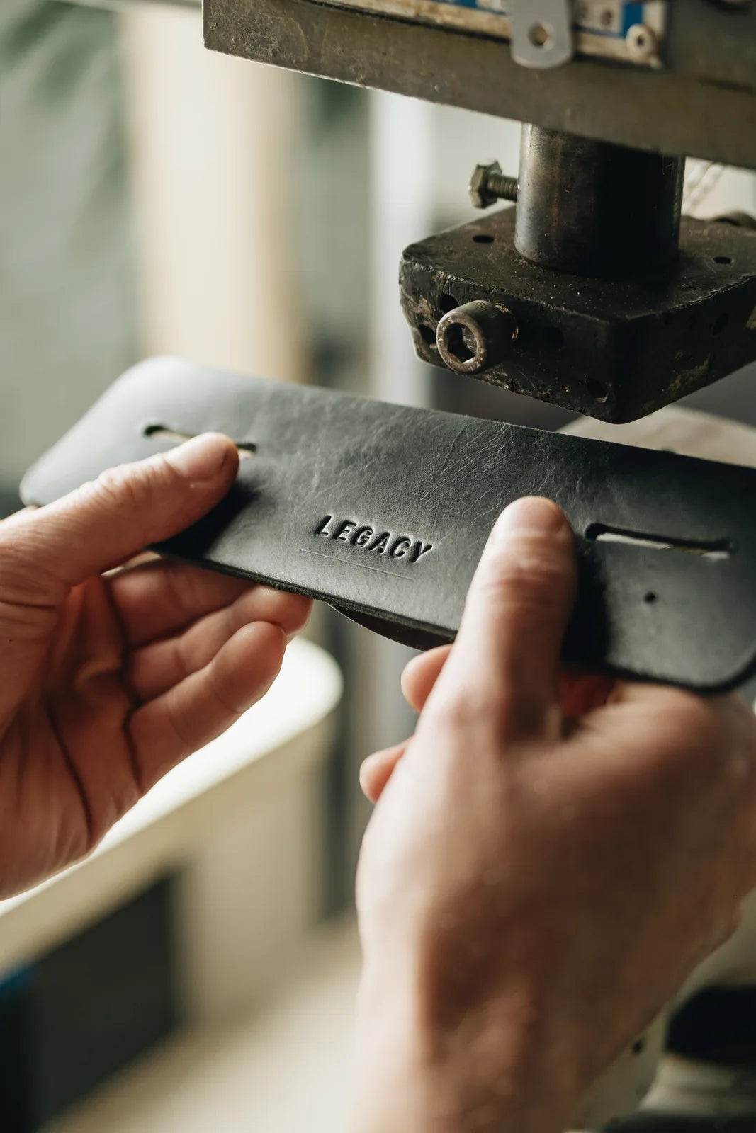 A maker holding an embossed Legacy leather component at the workshop press