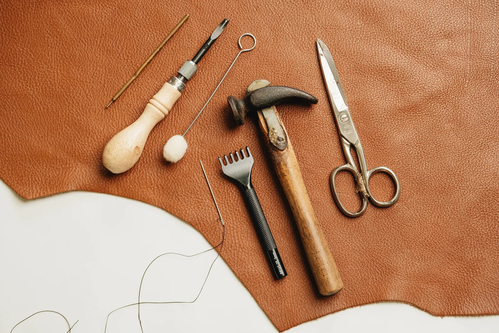 Scissors, a hammer, thread and hand tools on a leather-covered workbench