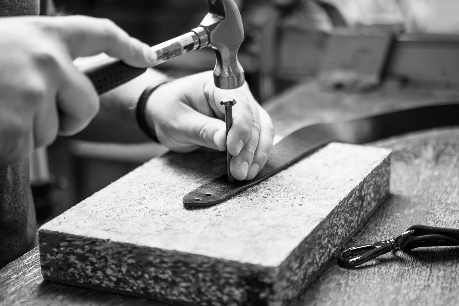 A maker working a leather component with a hammer and hand tool