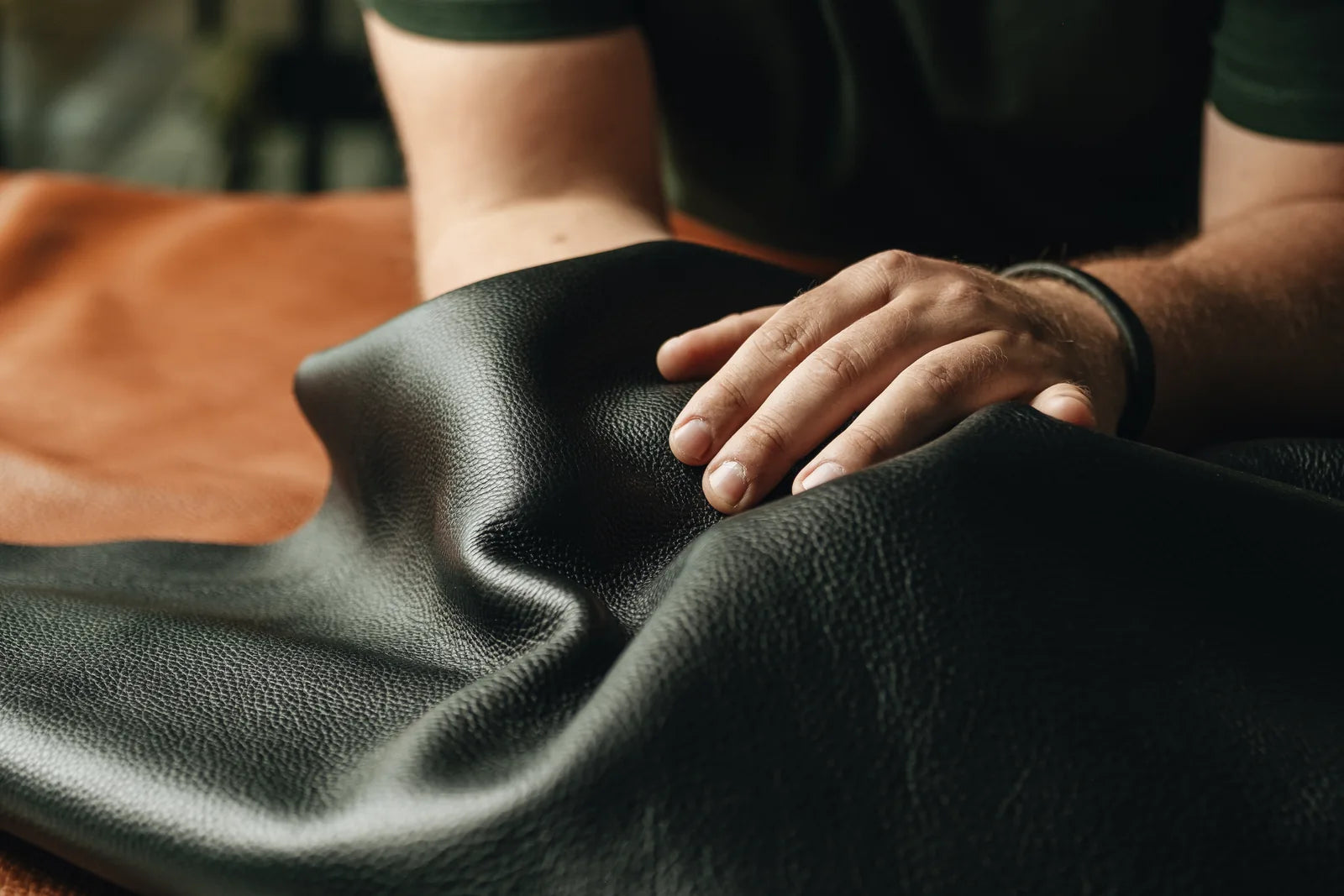 A hand moving across the grain of a dark leather hide