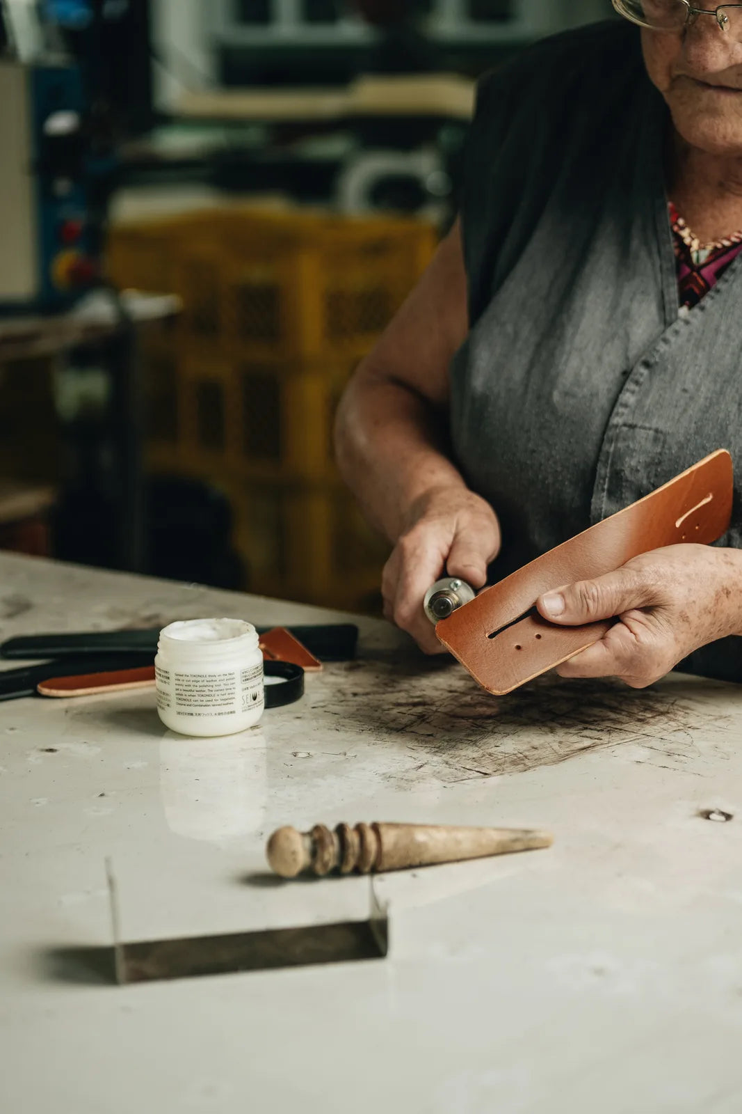 A maker working on a narrow leather component at a workshop table