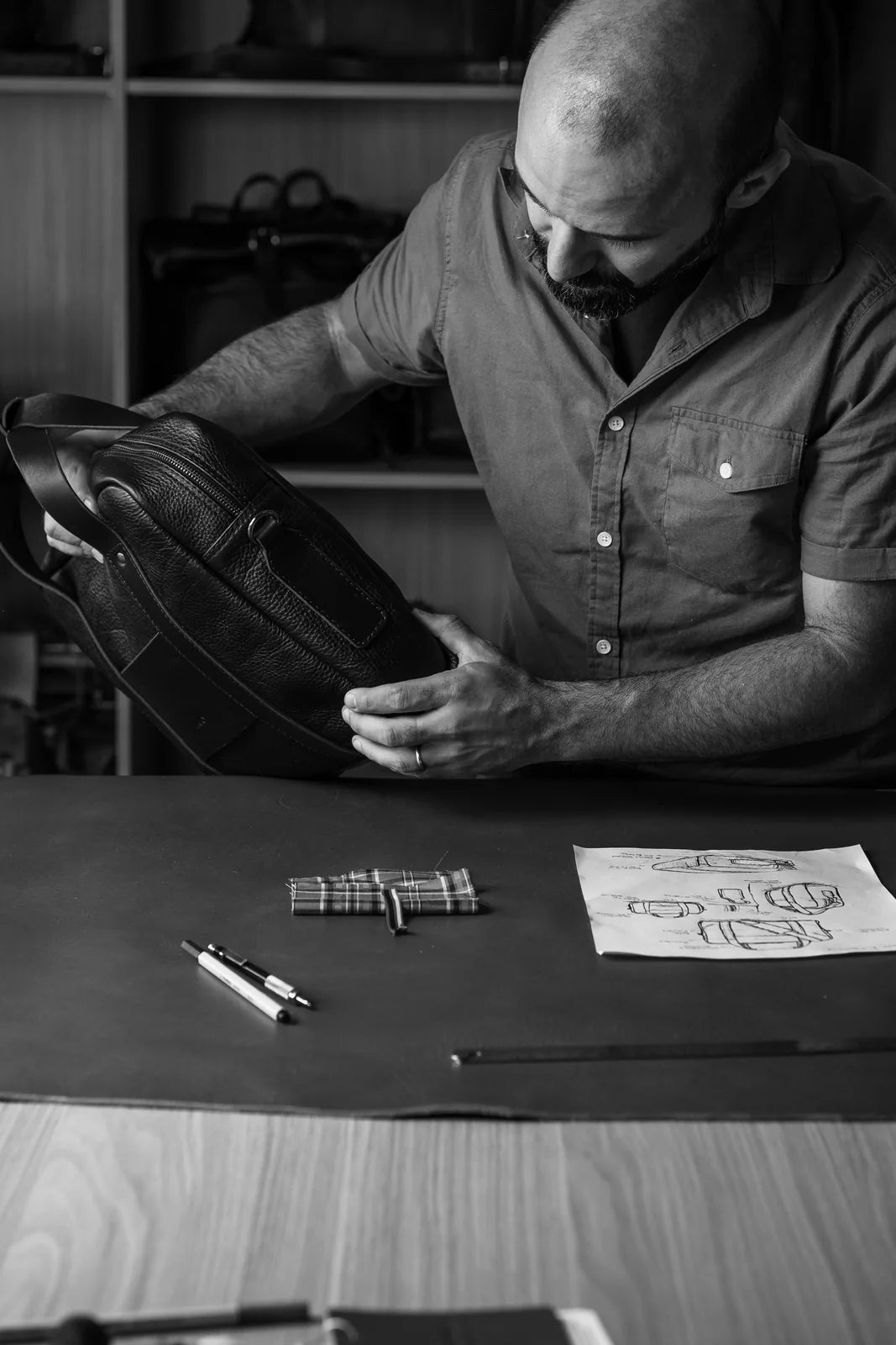 A seated maker examining a leather bag at the workshop table