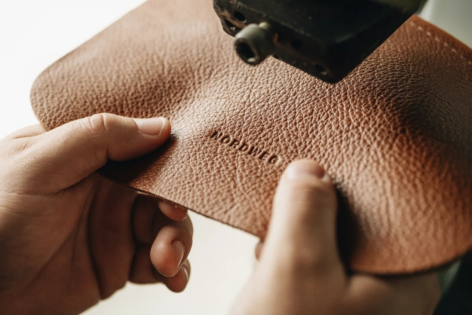 Hands holding a caramel leather component beneath the Legacy embossing press