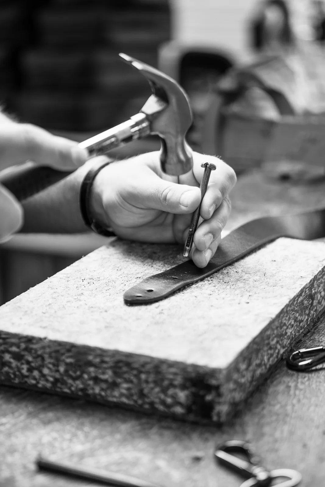 Hands working a leather component with a hammer and setting tool
