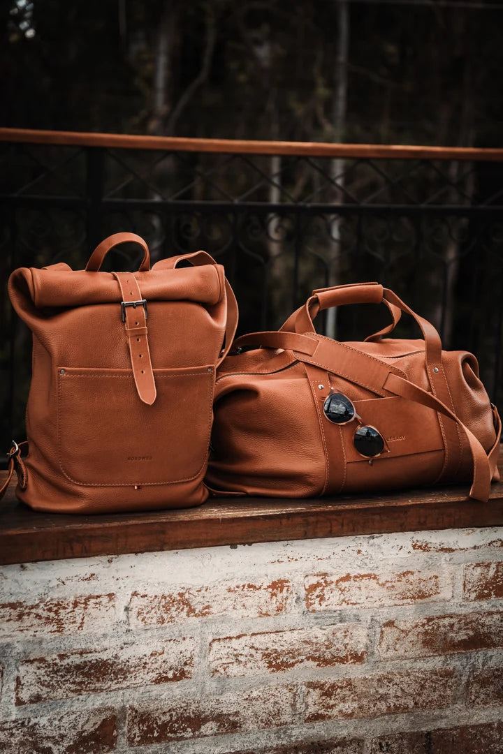 Cognac Legacy backpack and duffel together on a stone bench