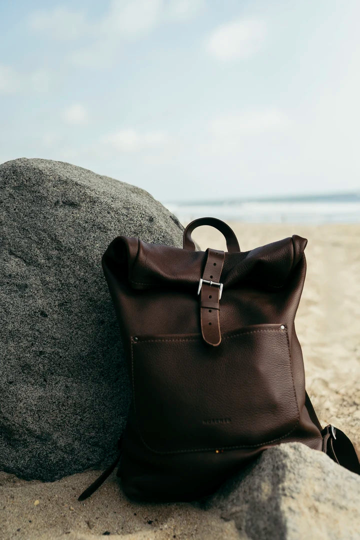 Espresso Legacy backpack beside a rock on a sunny beach