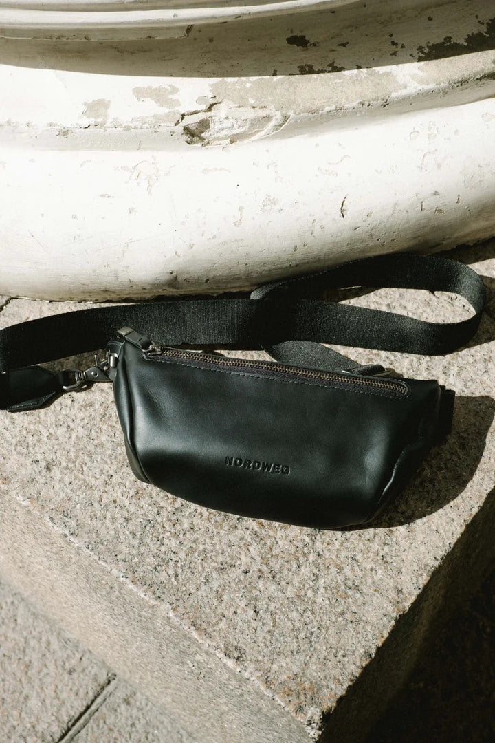 Black Pulse sling bag resting on stone steps in sunlight